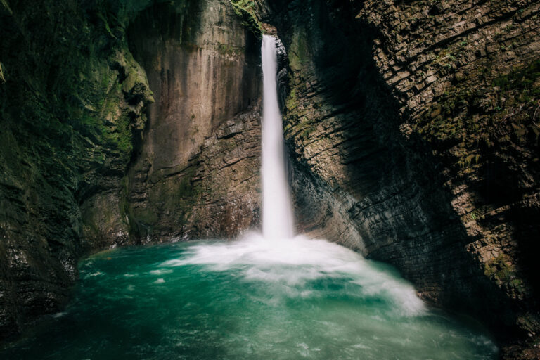 A narrow waterfall drops into a turquoise pool inside a canyon