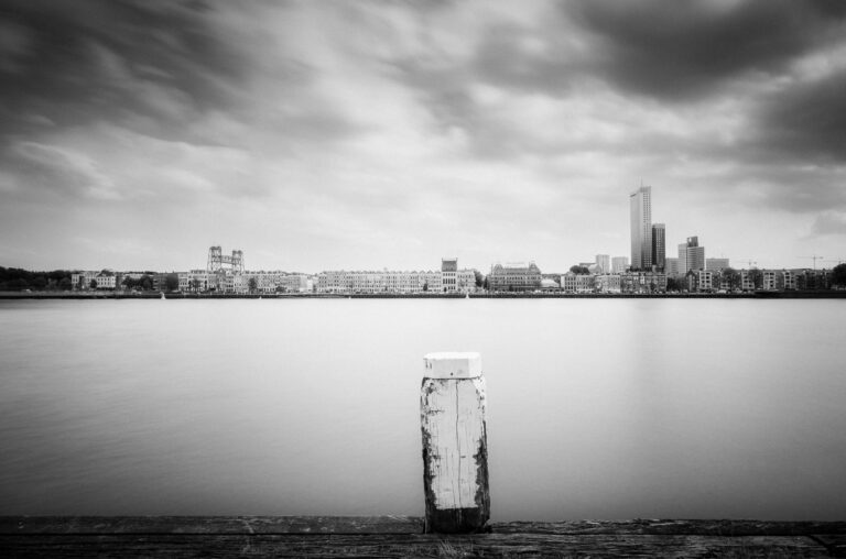 A weathered mooring post facing the Rotterdam skyline