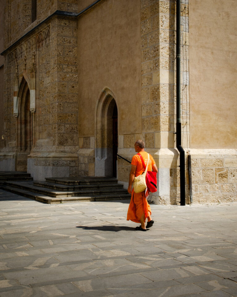 A figure in orange walks past a church under bright sun